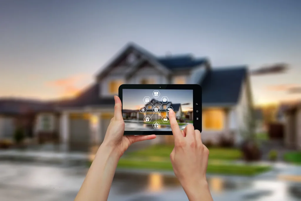 Hands holding a tablet with a smart home security and automation app, superimposed over a blurry image of a house at dusk.